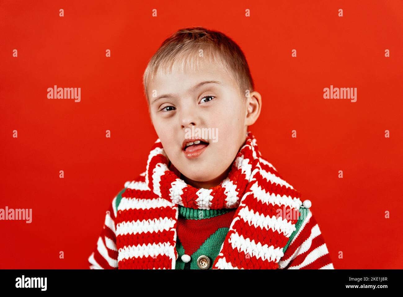 Happy child with Down syndrome in Christmas scarf having fun and laughing in studio. Christmas mood. happy new year. Portrait on red background Stock Photo