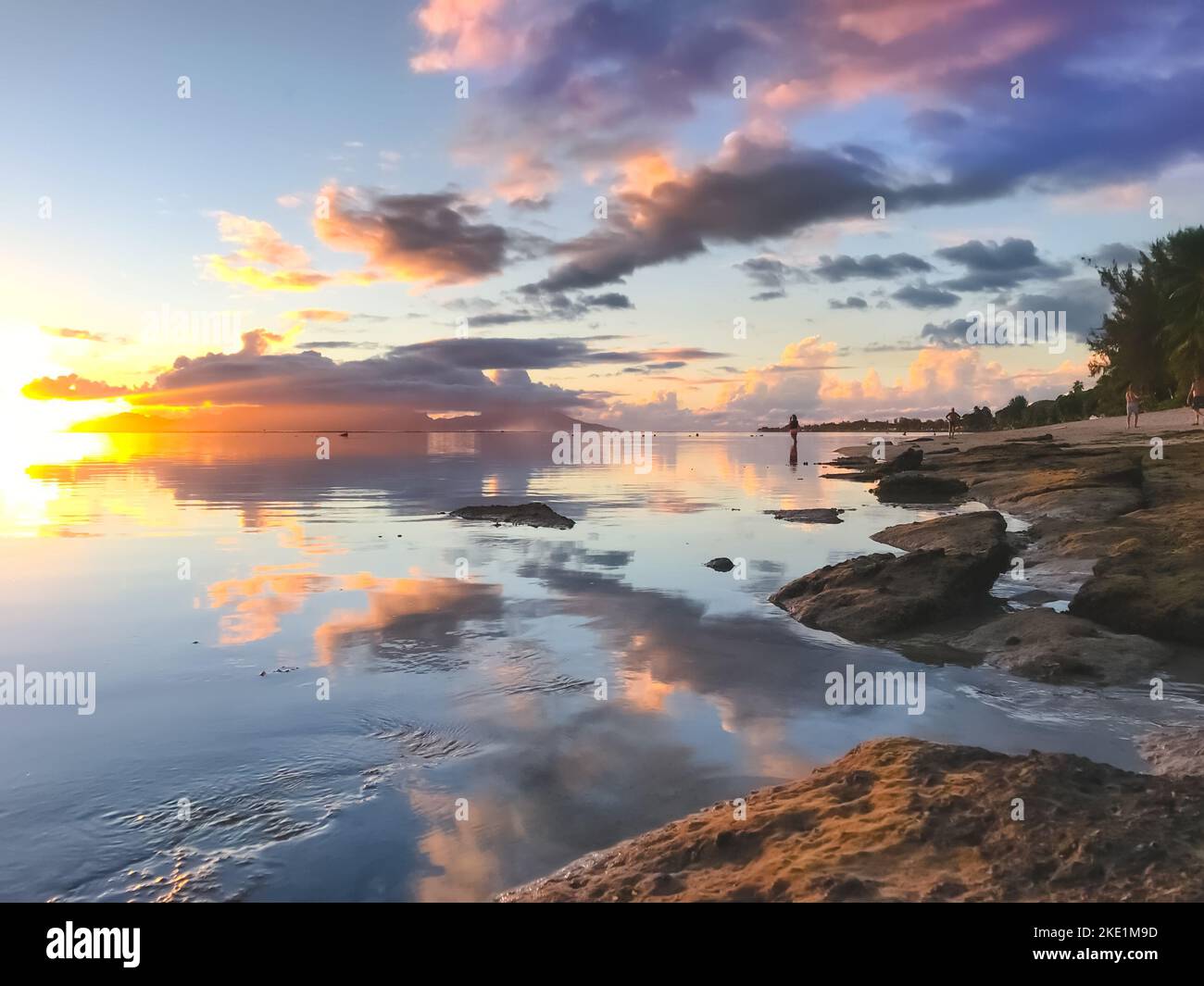 Bright tropial sunset reflected in ocean water. Colorful clouds in sky and rocky seashore. Amazing natural summer scenery. Wonderful Nature landscape during sunset. Travel, tourism, relax. Stock Photo