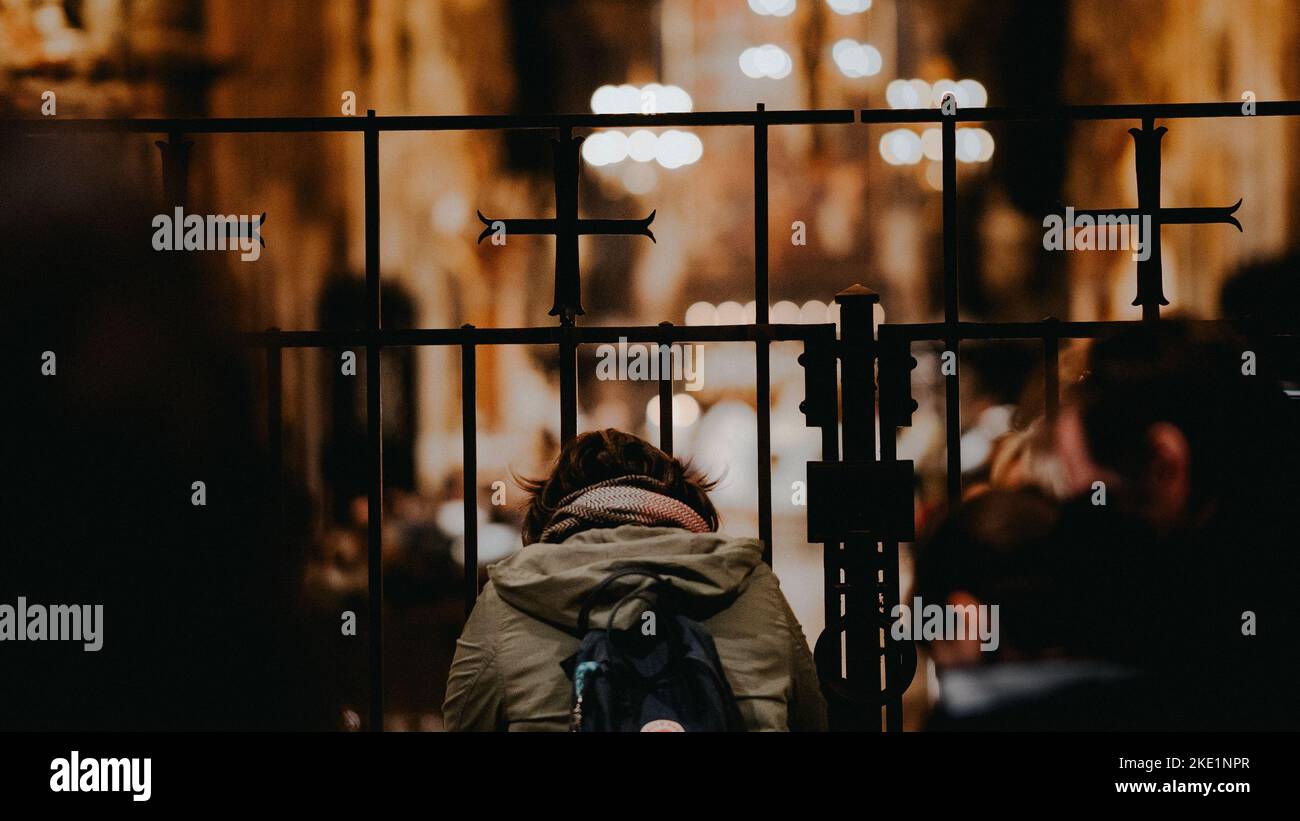 A woman from the back is bowing humbly behind fence during her pray in
