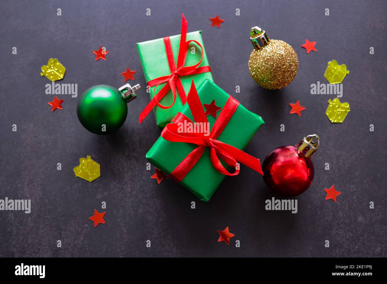 Gifts in green paper with red and yellow ribbons, gold, red and green christmas balls and confetti in the form of red stars. Black background. Big sal Stock Photo