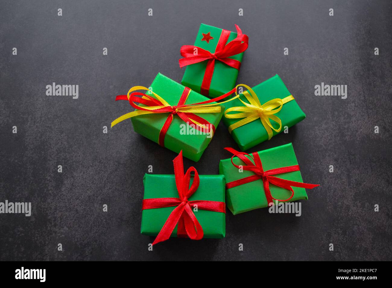 Gifts in green paper with red and yellow ribbons lie next to each other in the form of a Christmas tree with a red star on top. Black background, copy Stock Photo
