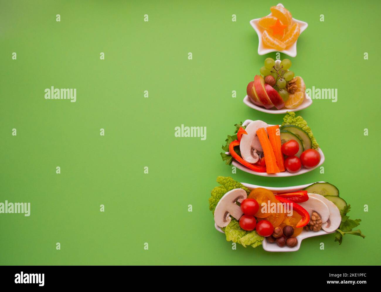 Plate in the form of a Christmas tree with vegetables, fruits, mushrooms and berries.Green background. The concept of vegetarian treats for the holida Stock Photo