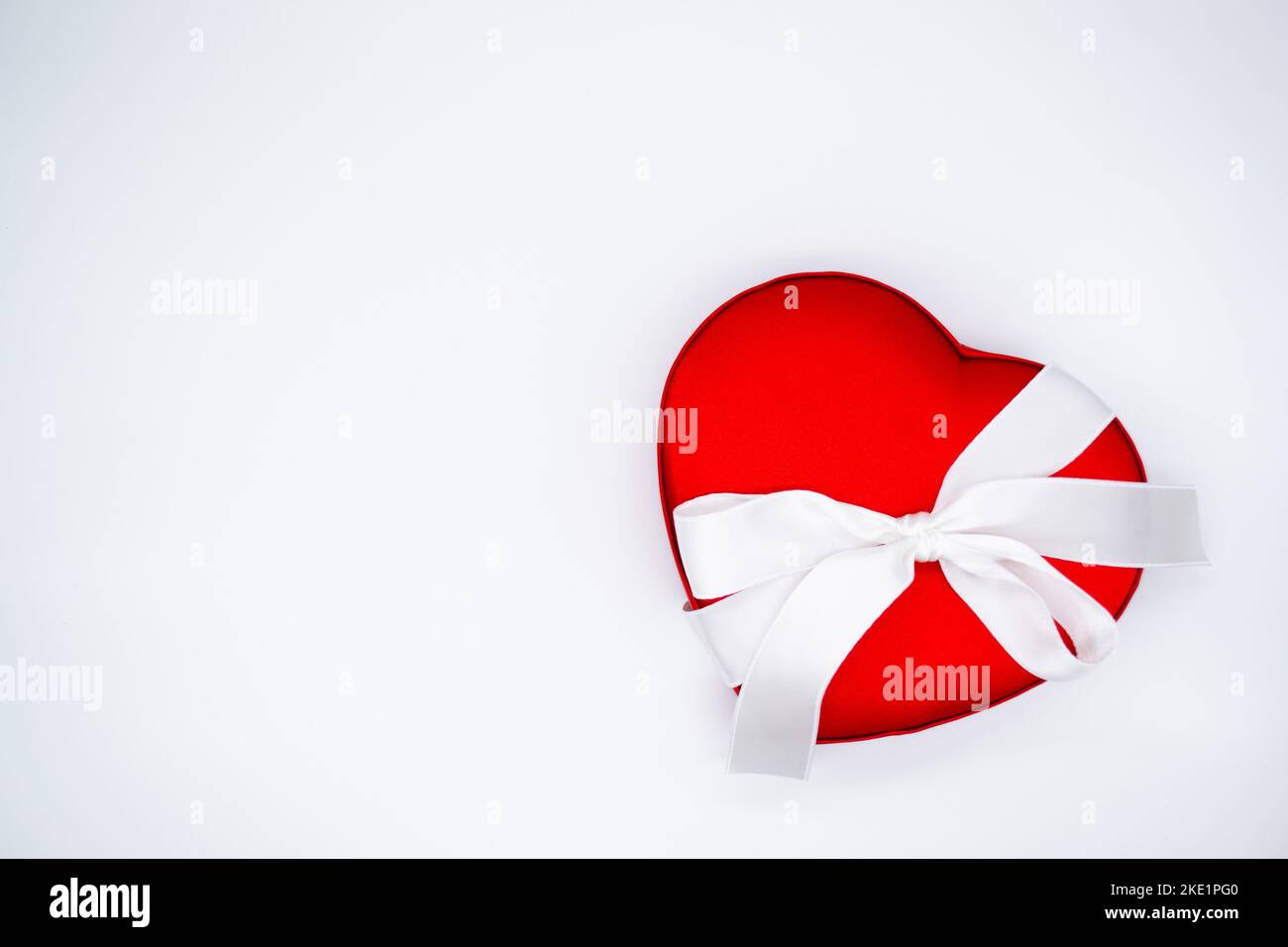 Bright red satin box in the shape of a heart, tied with a white ribbon with a bow on a white background. Concept of love, Valentine's day, gift, belov Stock Photo