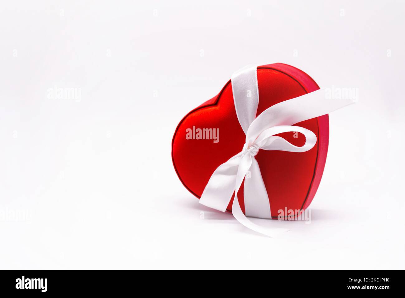 Bright red satin box in the shape of a heart, tied with a white ribbon with a bow on a white background. Concept of love, Valentine's day, gift, belov Stock Photo