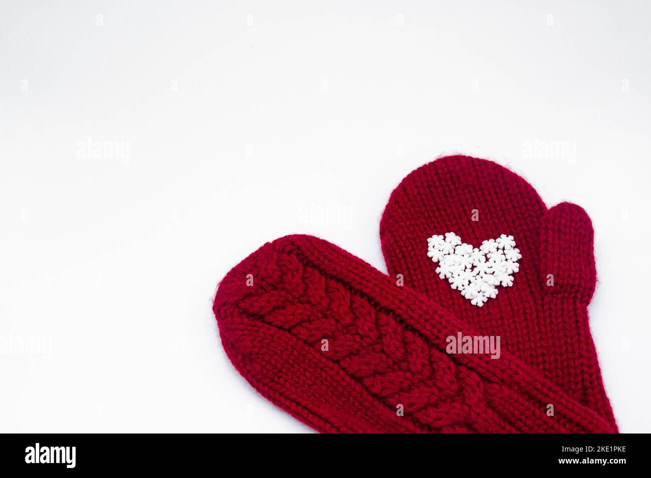 Two knitted red mittens lie one each other with white snowflakes in the shape of a heart. White background, isolated. Concept of Christmas, winter, lo Stock Photo