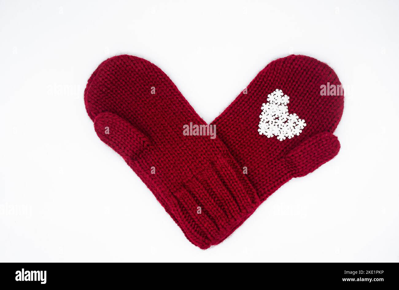 Two knitted red mittens lie one each other with white snowflakes in the shape of a heart. White background, isolated. Concept of Christmas, winter, lo Stock Photo