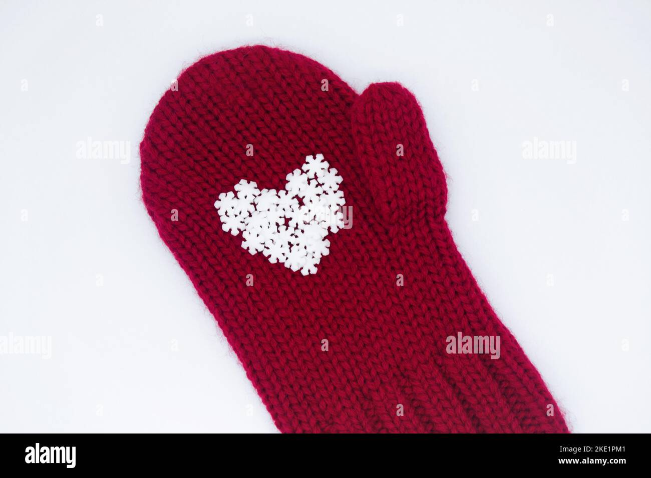 A knitted red mitten, on which white snowflakes in the shape of a heart lie as if in the palm of your hand on a white background, isolated. Concept of Stock Photo