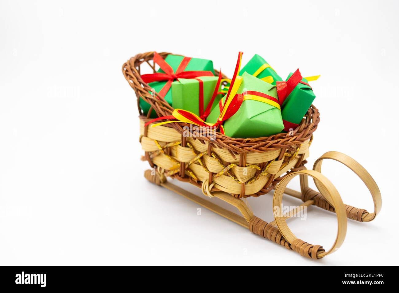 Old-fashioned wicker Santa sleigh with Christmas gifts wrapped in green paper with red ribbon. Stock Photo