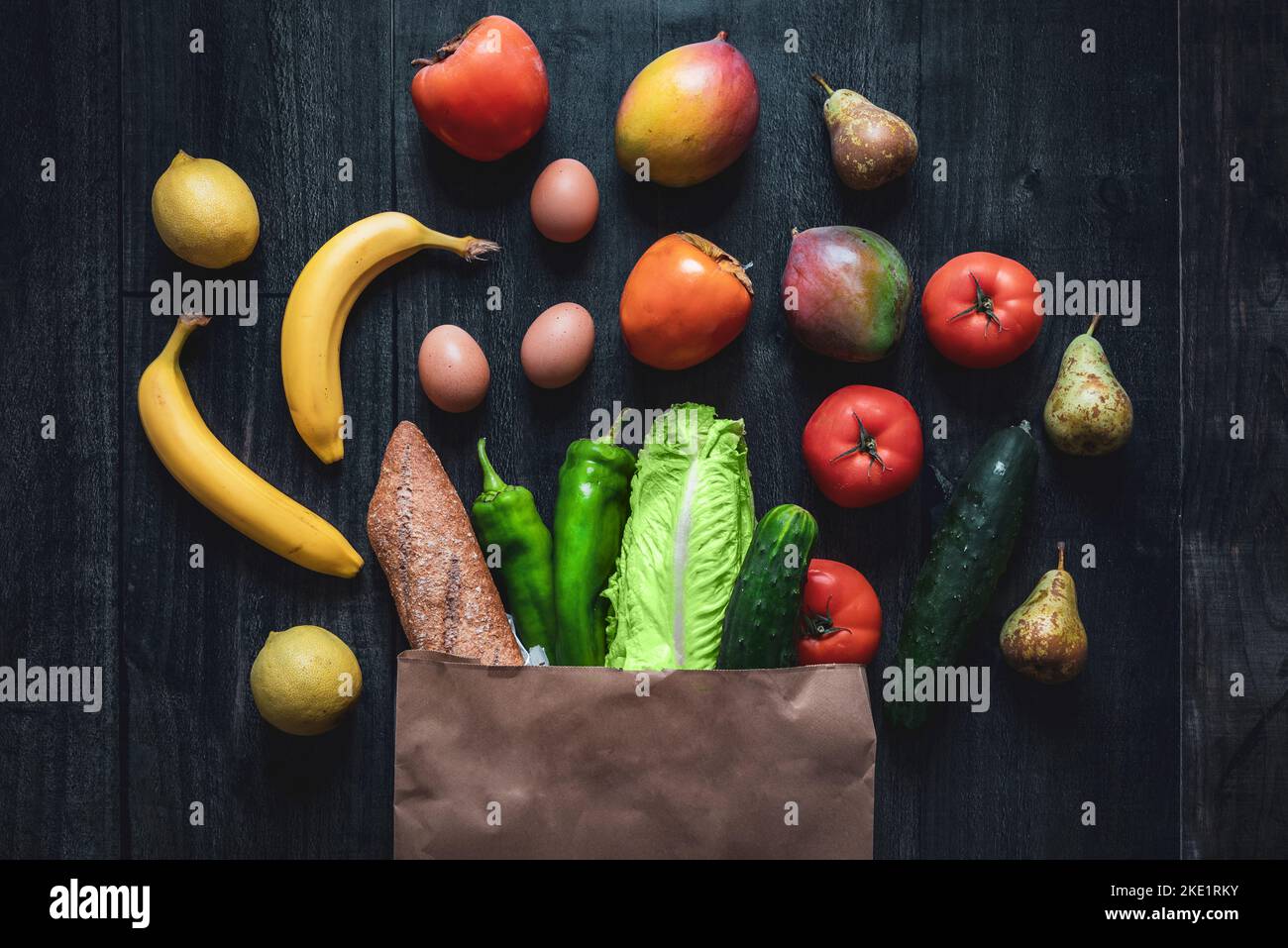 Shopping bag full of vegetables, fruits, eggs and bread on wooden background. Dark food photography. Rising prices of basic foodstuffs Stock Photo
