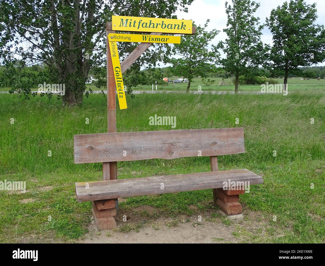 The view of a wooden ridesharing bench with signs in the greenery of