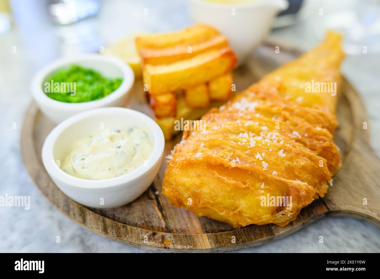 The British traditional fish and chips with mashed peas and tartar sauce on a wooden board. Stock Photo