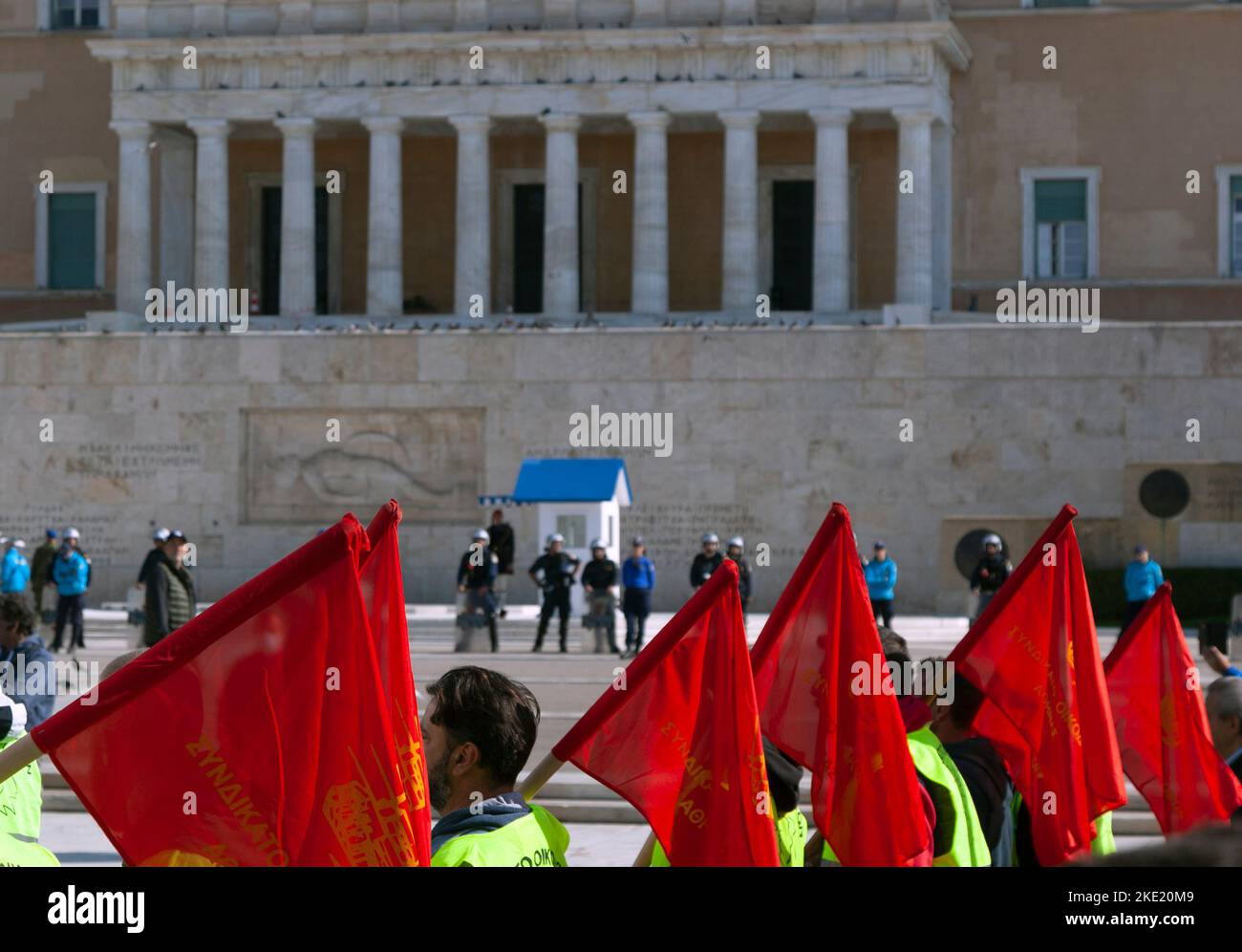 Protesters holding red flags are passing by the Greek Parliament, which is guarded by police forces, during a mass demonstration against government. Stock Photo