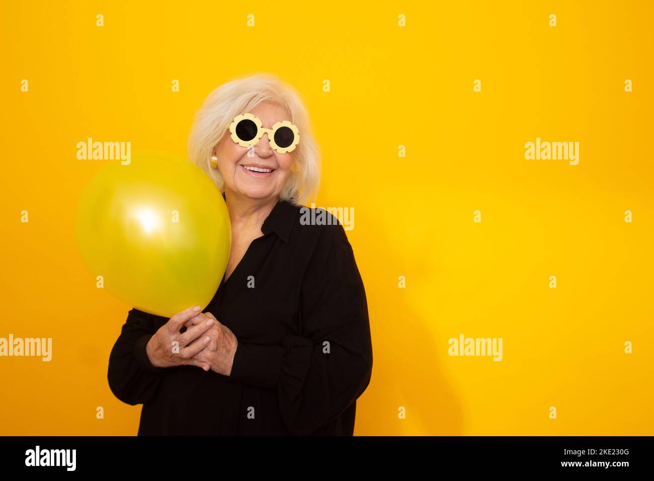 older woman smiling with funny sunglasses holding a balloon Stock Photo