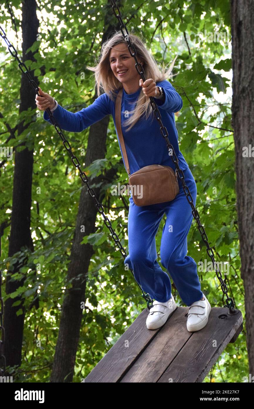 Attractive Blonde Girl Rides On A Carousel Swing In A Blue Suit With A Handbag And Smiles Stock