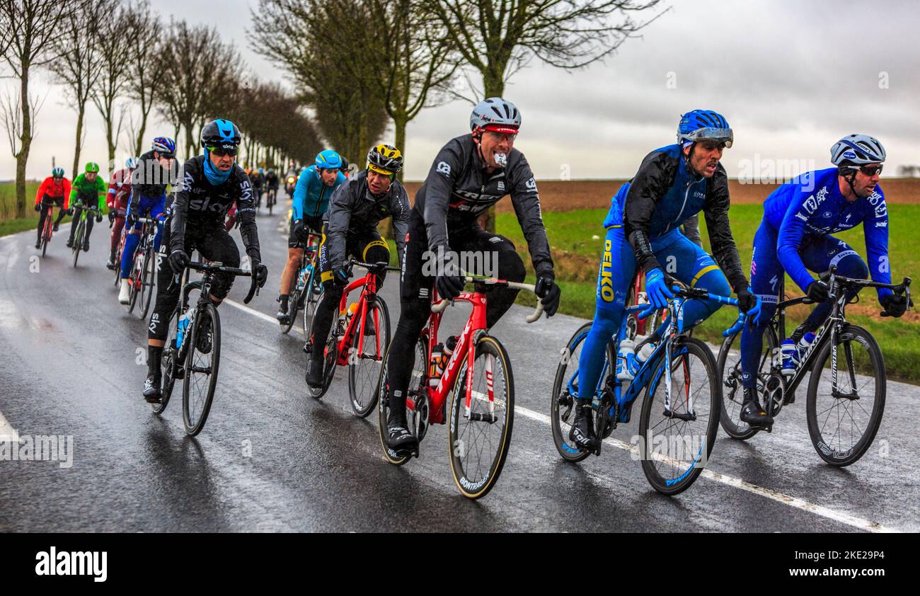 Angerville, France - March 6, 2017: The peloton riding on a wet road ...