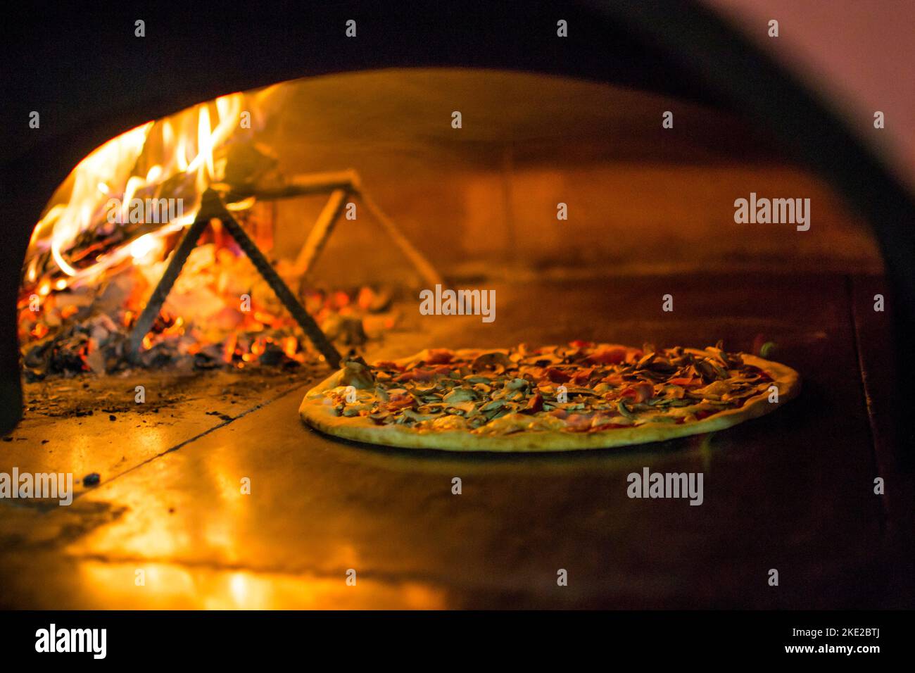 cooking pizza in the oven . Pizza near the stone stove with fire. Background of a traditional pizzeria restaurant with a fire place. Stock Photo