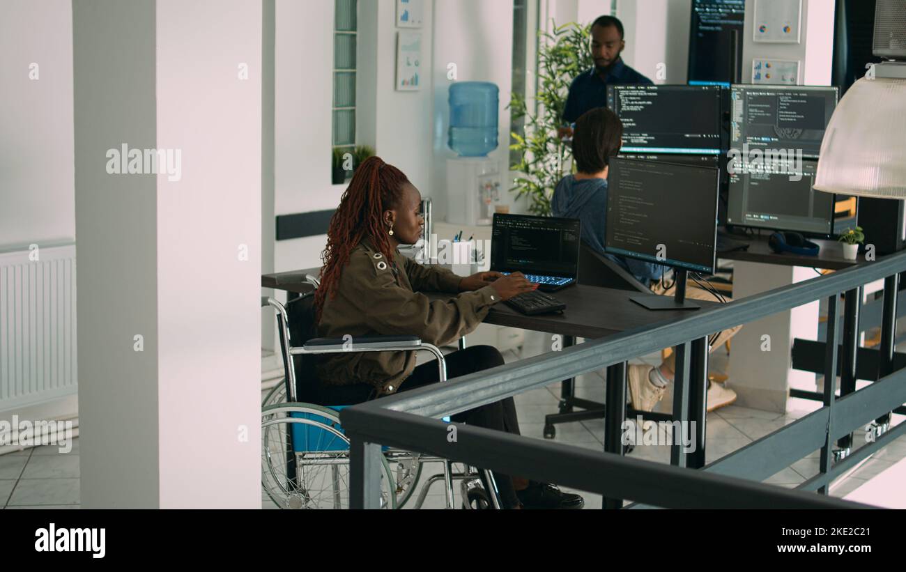 African american app developer in wheelchair analyzing software program, coding html script with it web language. System programmer with impairment coding new server interface. Stock Photo