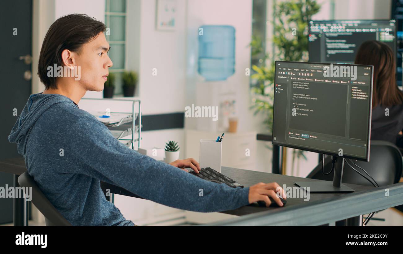 Asian programer developing database interface and writing server code, working in software development office. System engineer creating algorithm on terminal window. Handheld shot. Stock Photo