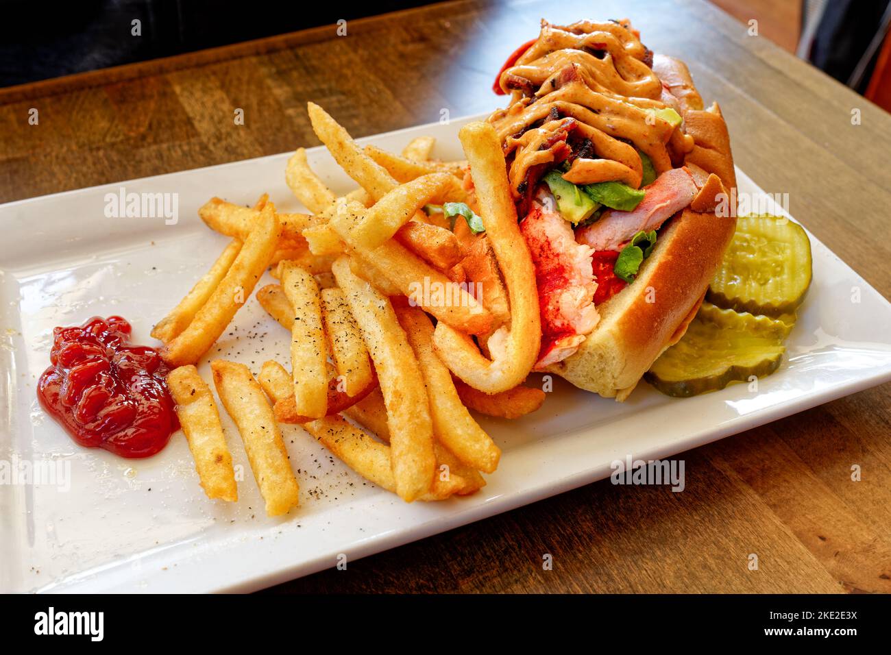 Lobster sandwich with avocado and southwest mayo on a white plate with french fries and ketchup Stock Photo