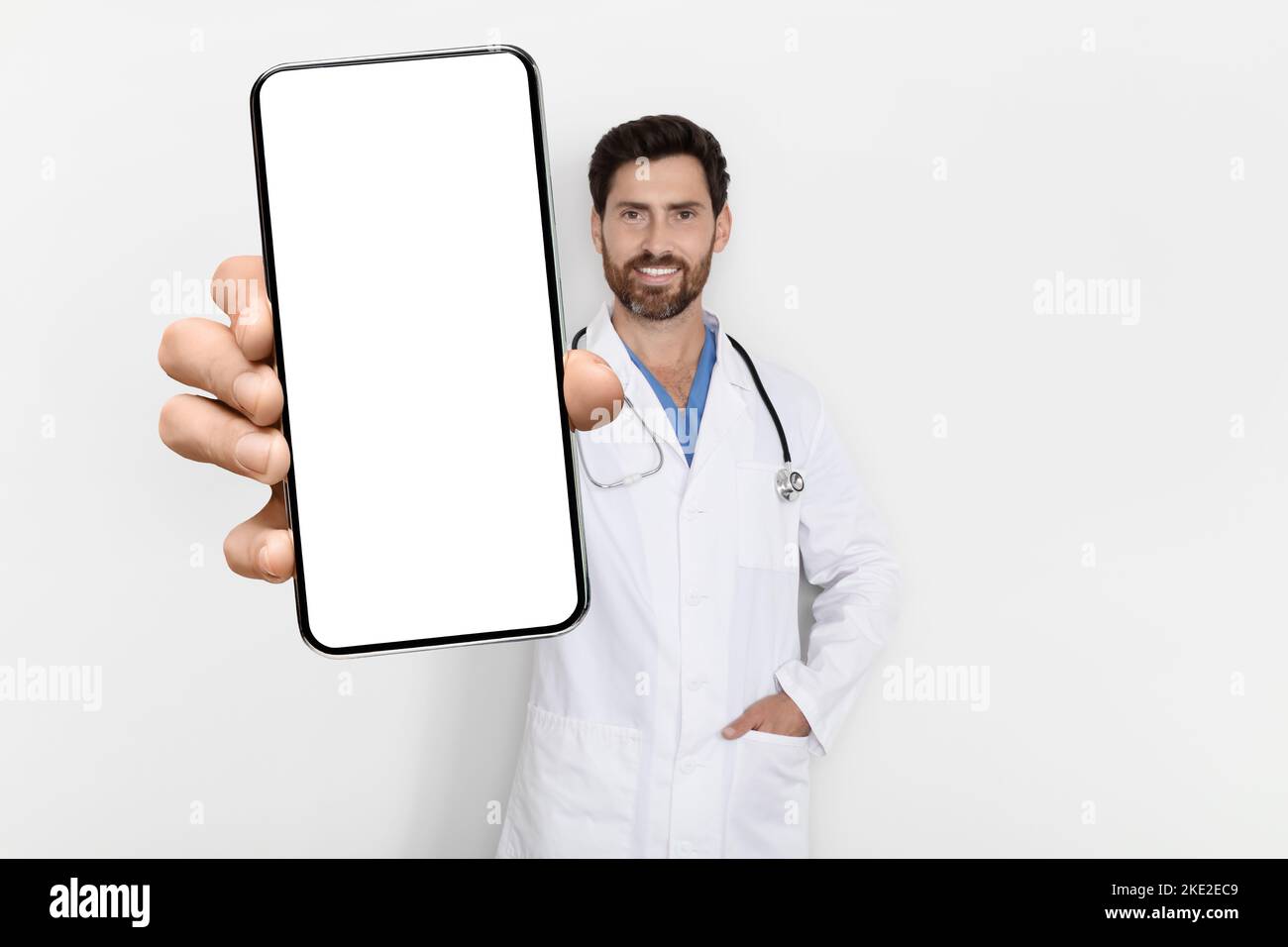 Medical App. Handsome Male Physician In Uniform Demonstrating Big Blank Smartphone Stock Photo