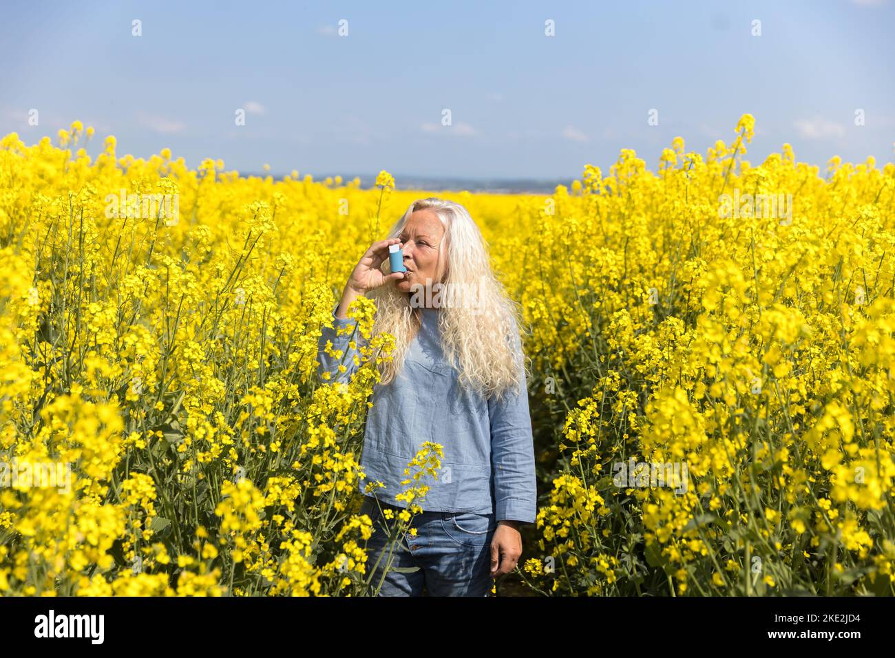 Elderly woman using an asthma metered dose inhaler in a blooming canola field Stock Photo