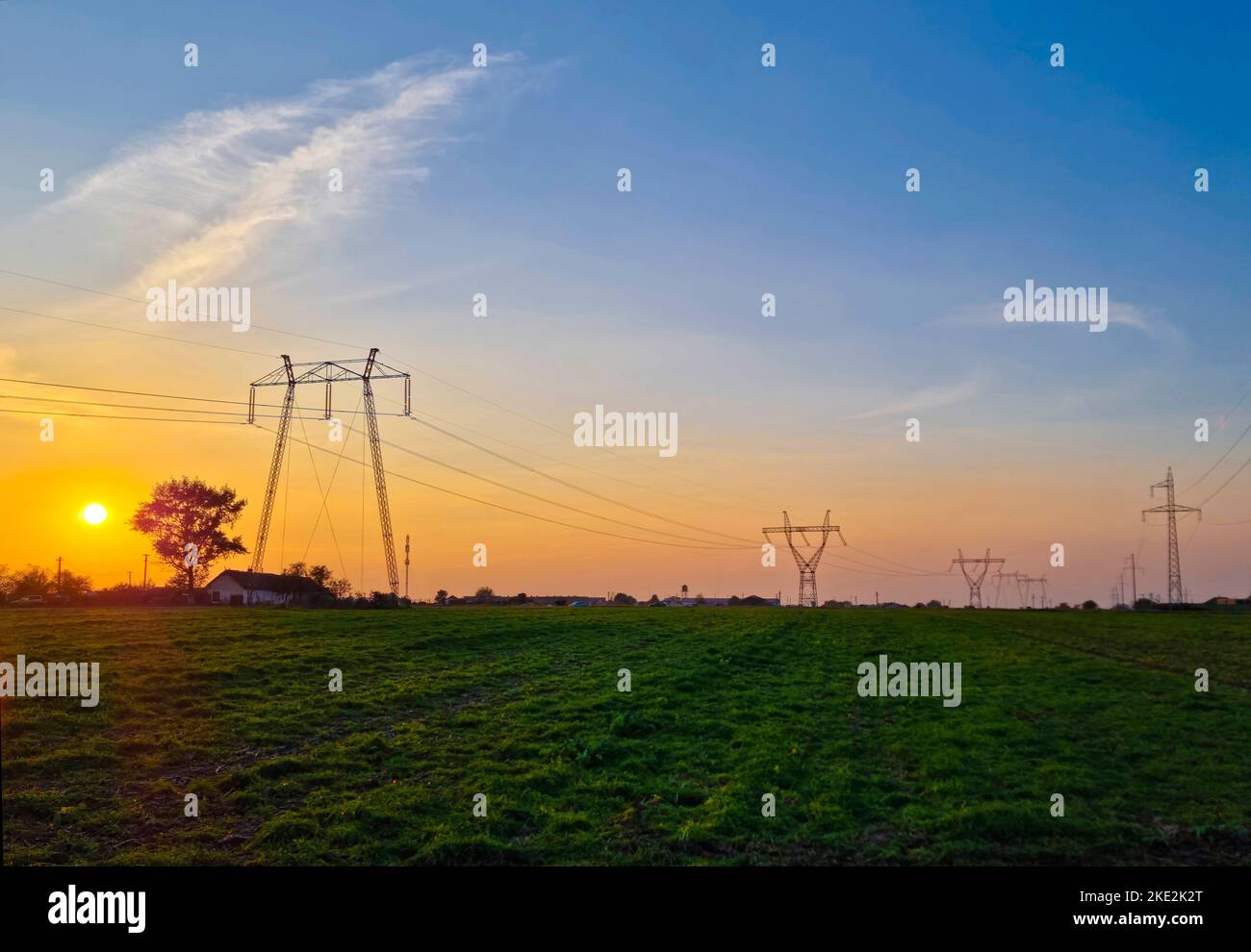 High voltage electric poles, rural landscape with power pylons in a row, at sunset Stock Photo