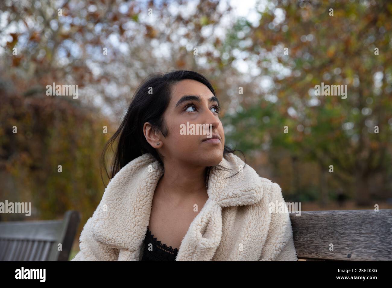 Single indian young girl seated on a bench at public park looking at the sky. Stock Photo