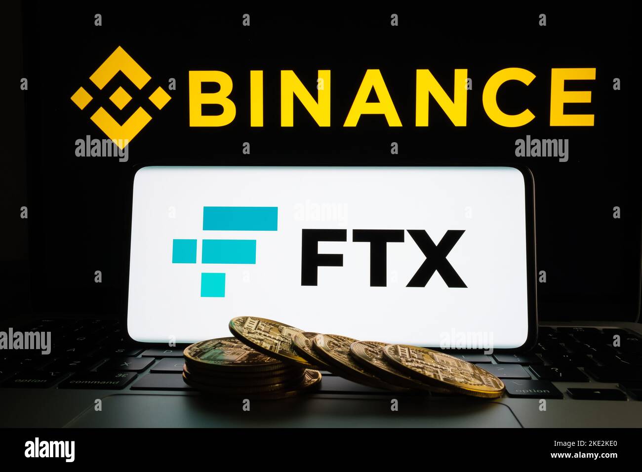 Binance and FTX Cryptocurrency Exchange merger concept. FTX logo seen on smartphone, fallen stack of bitcoin tokens, Binance logo on a laptop. Staffor Stock Photo