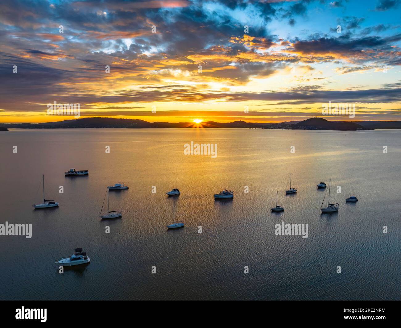 Sun rising over Brisbane Water with clouds and boats at Koolewong and Tascott on the Central Coast, NSW, Australia. Stock Photo