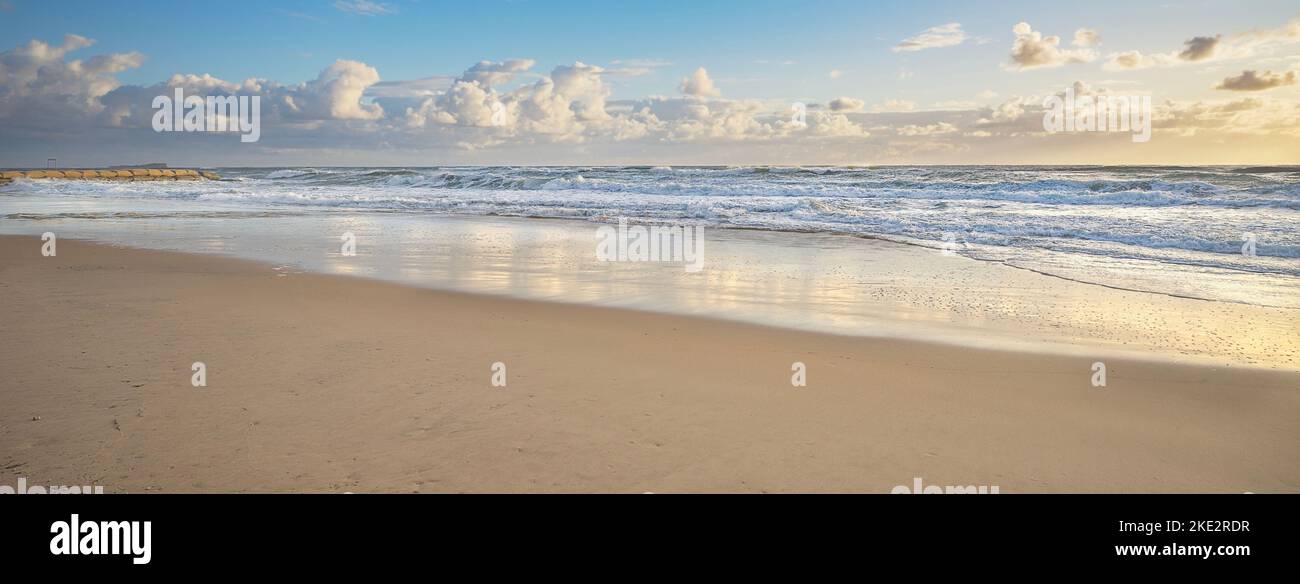 Panoramic view of Cotton Tree surf beach in the golden glow of the early morning after sunrise. The waves are rough and breaking fiercely on the sandy Stock Photo