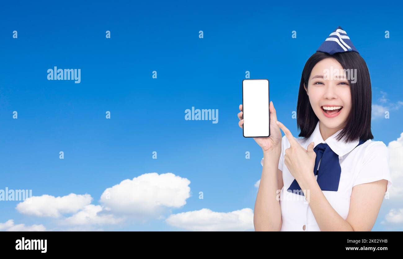 Beautiful Airline stewardess showing the mobile phone with blank screen on cloud background Stock Photo