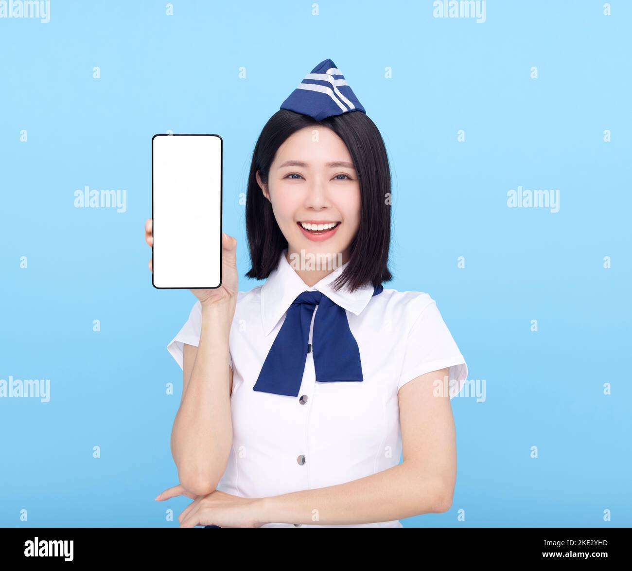 Beautiful stewardess showing the mobile phone with blank screen on blue background Stock Photo