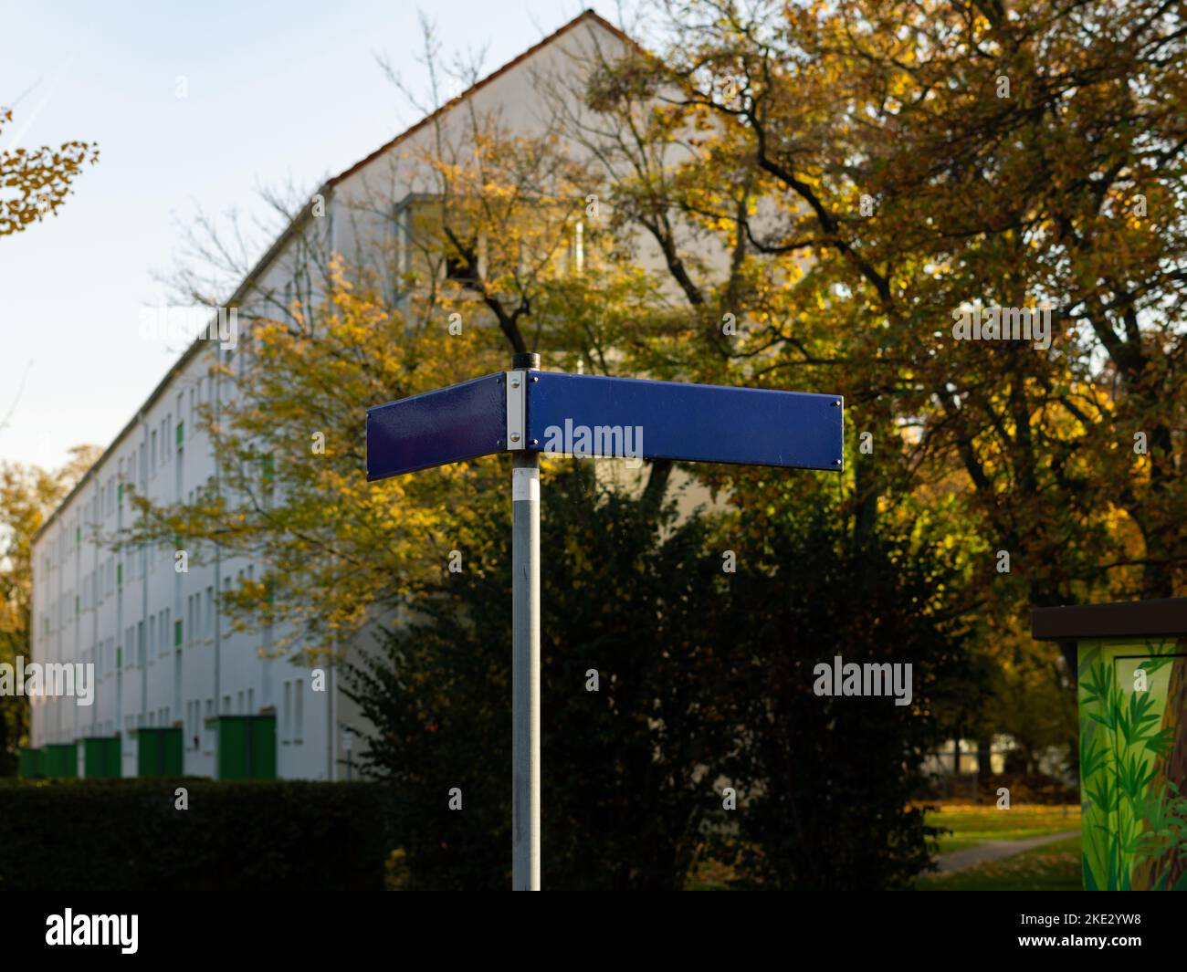 Blank road name signs at a corner in a residential district. Blue metal plates on a signpost as a template or copy space. Autumn leaves on the trees. Stock Photo