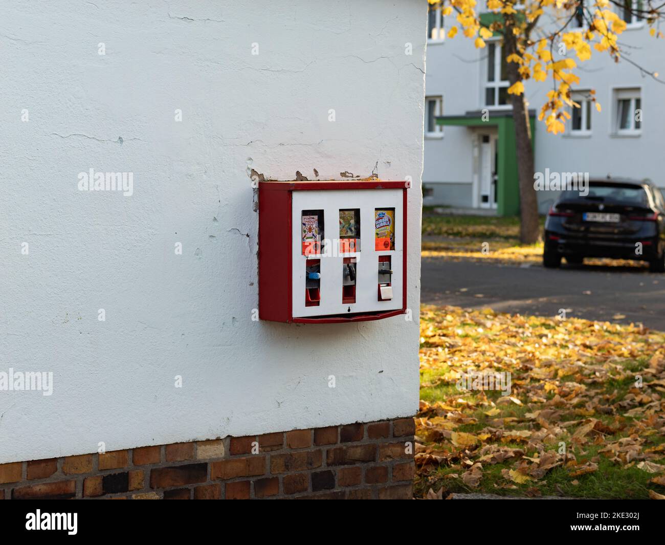 Red chewing gum vending machine on a wall in a residential district. Candy and cheap toys for children. The vintage machine works with Euro coins. Stock Photo
