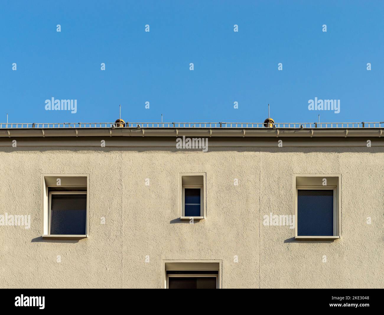 Symmetric facade of a residential house. White wall plaster with windows on the building exterior. Looking up to the roof gutter and the blue sky. Stock Photo