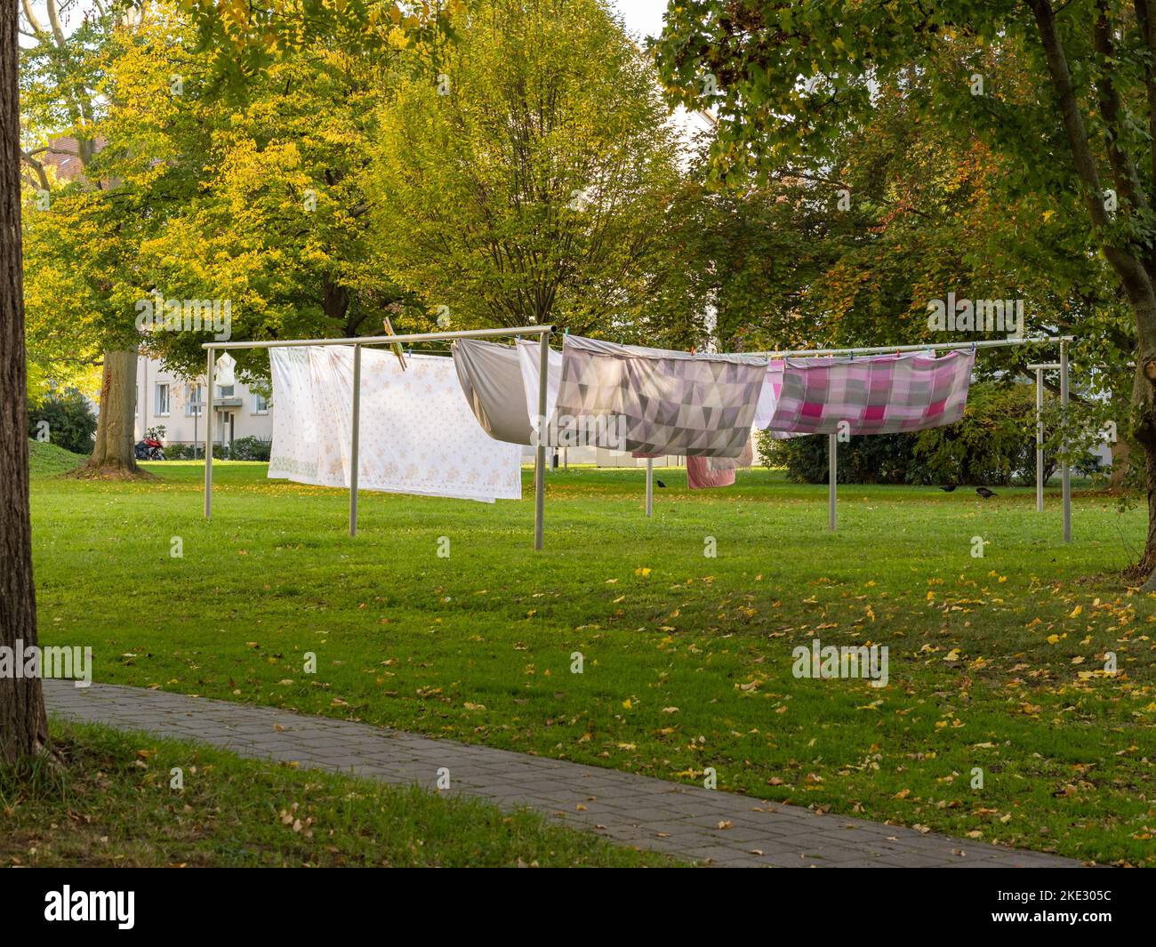 Laundry hanging on a clothesline in a backyard. Bed sheets and blankets drying outdoor in the wind. Housekeeping in a residential district. Stock Photo