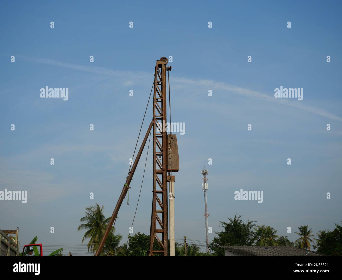 Concrete pile is being driven into the ground at construction site using piling machine with blue sky and white cloud in background Stock Photo