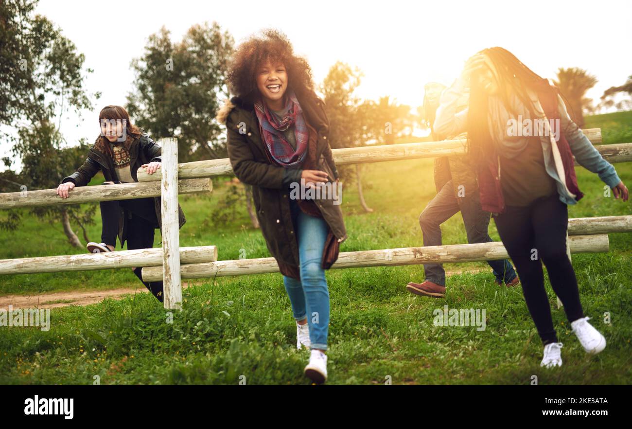 We just want to have fun. a group of friends jumping over a fence in a field for fun. Stock Photo