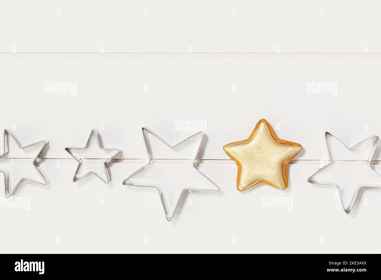 Cooking holiday cookies. Bakery flat lay. Ginger cookie in the form of stars, covered with gold glaze and cookie cutters on a white wooden background. Stock Photo