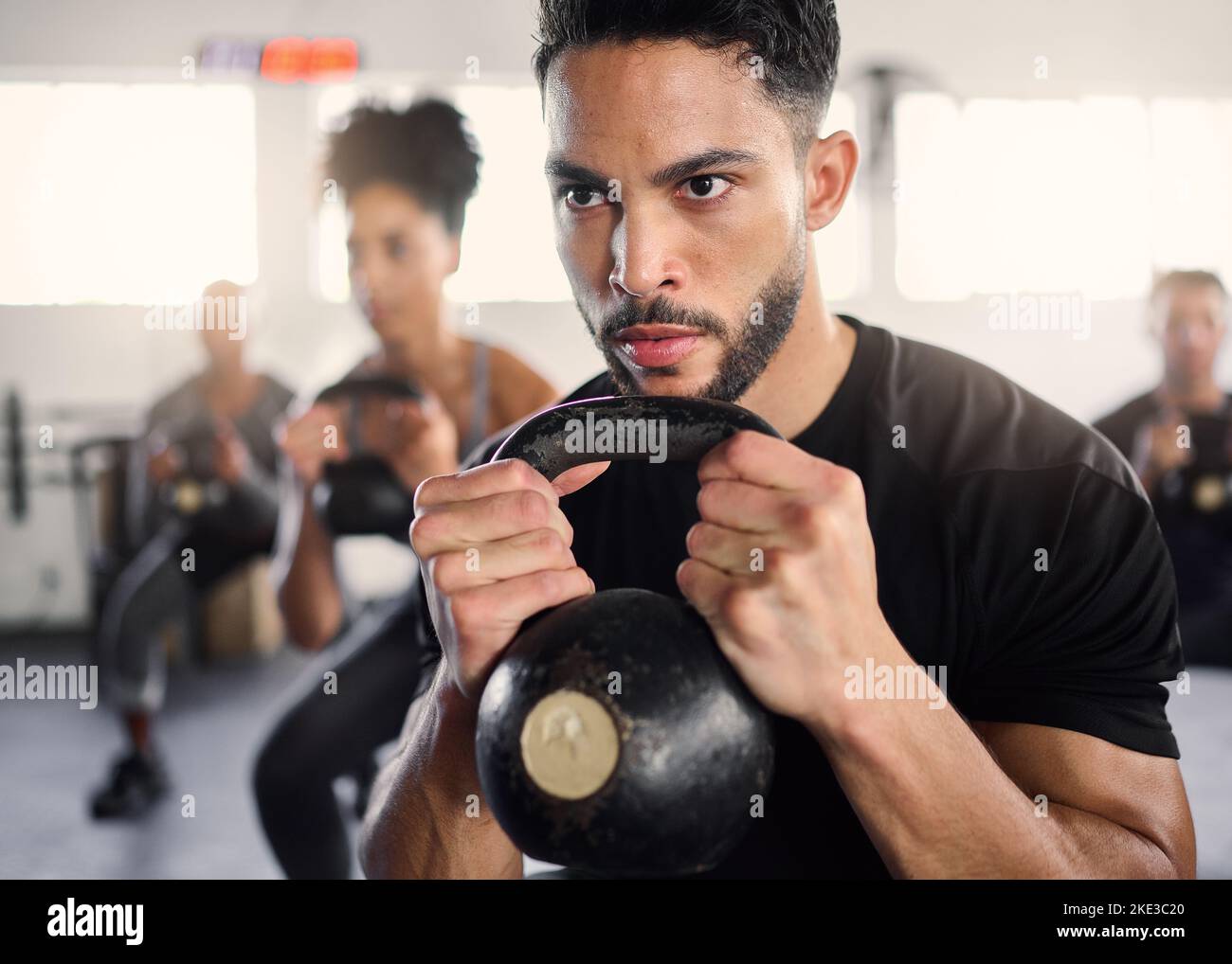 Strong man, personal trainer and group training with kettlebell squat exercise, workout and fitness in gym club. Bodybuilder coach teaching sports Stock Photo