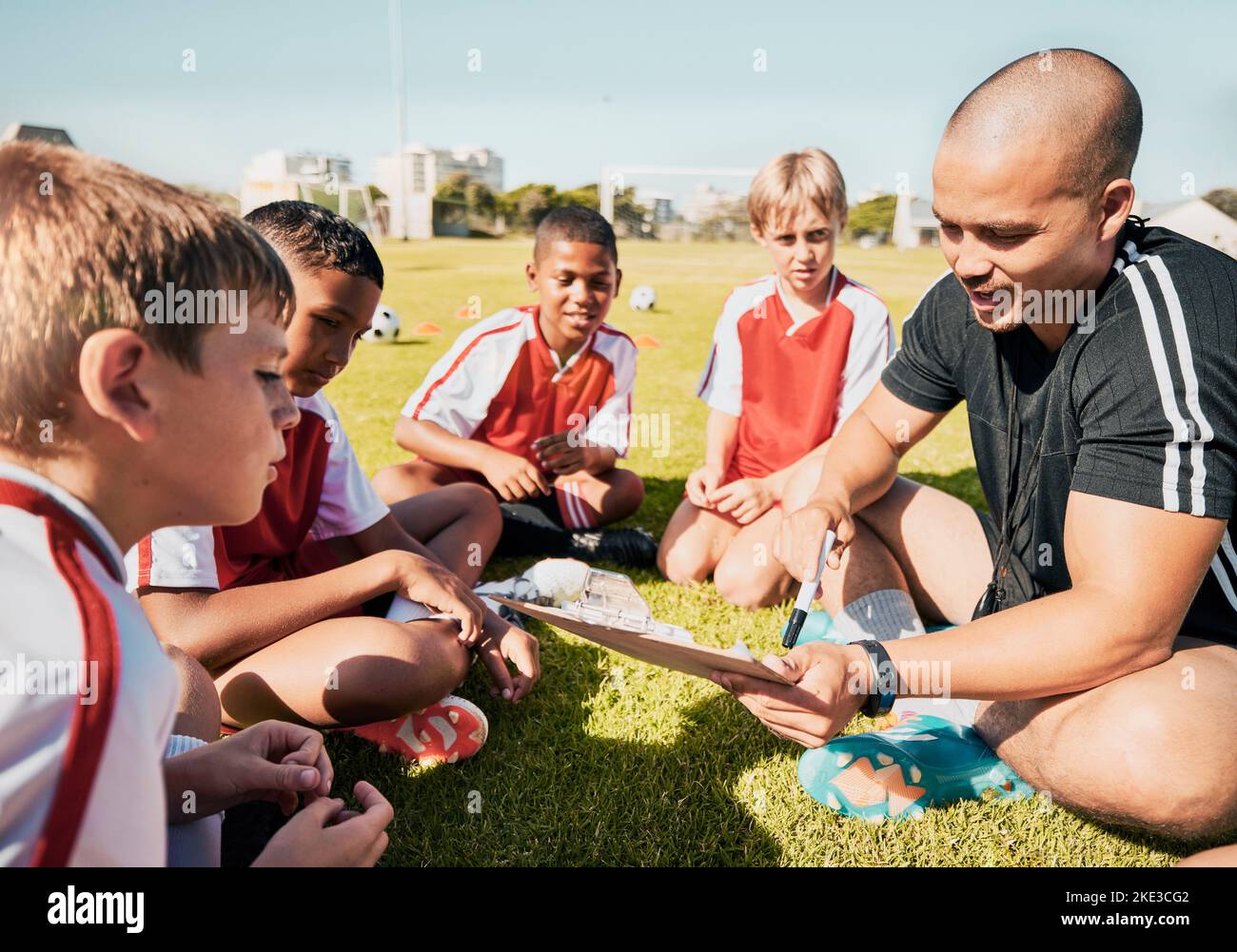 Soccer, football coach with team talk and strategy with tactics winning game sitting on grass training field. Boy children athletes, teamwork and Stock Photo