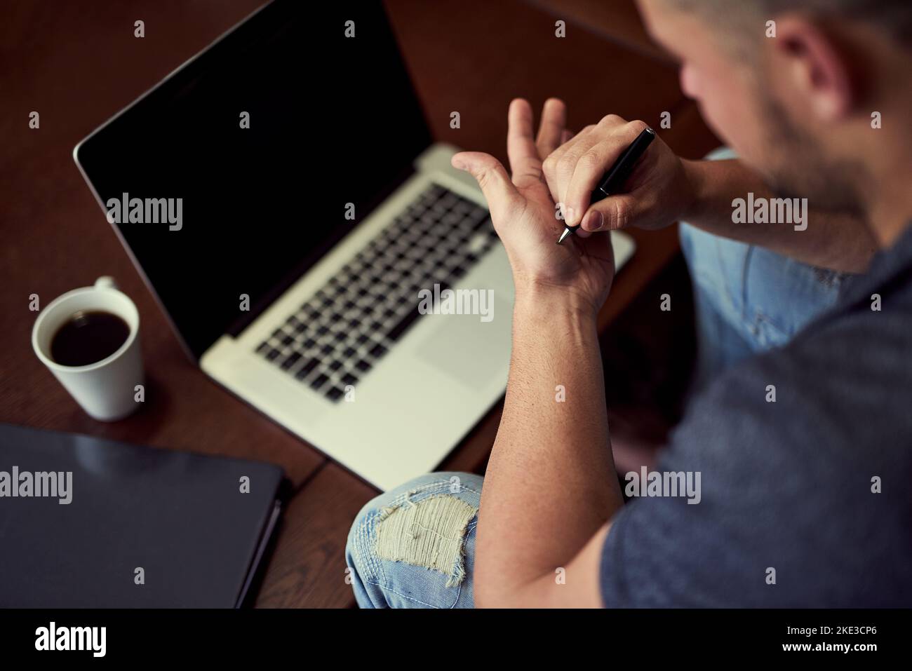 Probably not the best way to remember your password. an unidentifiable young man making notes on his hand while he works on his laptop at home. Stock Photo
