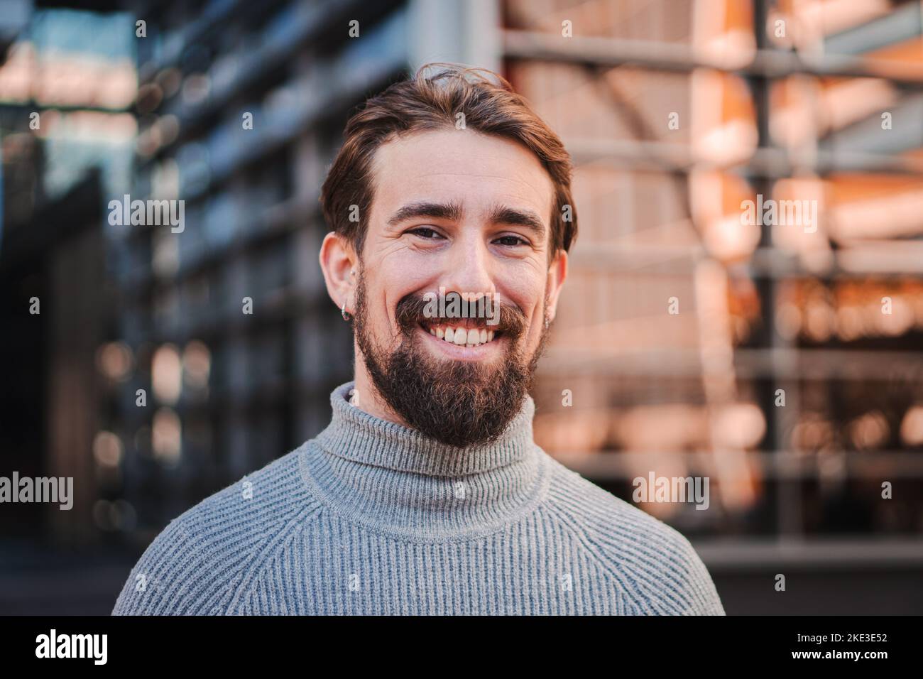 Close up portrait of awesome young caucasian male smiling and looking at camera at the background city office buildings Stock Photo