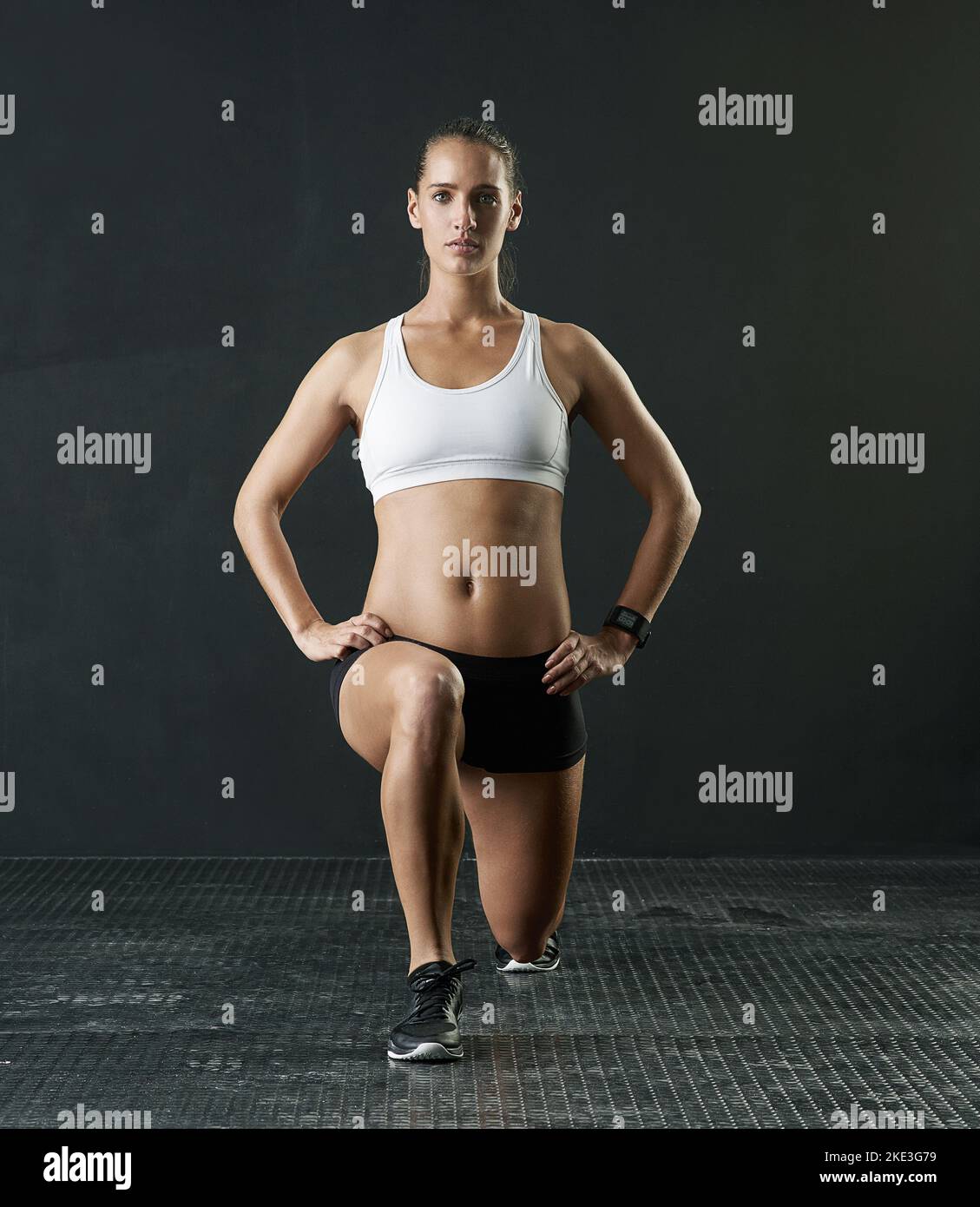 https://c8.alamy.com/comp/2KE3G79/lunging-her-way-towards-fitness-studio-portrait-of-an-attractive-young-woman-doing-lunges-against-a-dark-background-2KE3G79.jpg