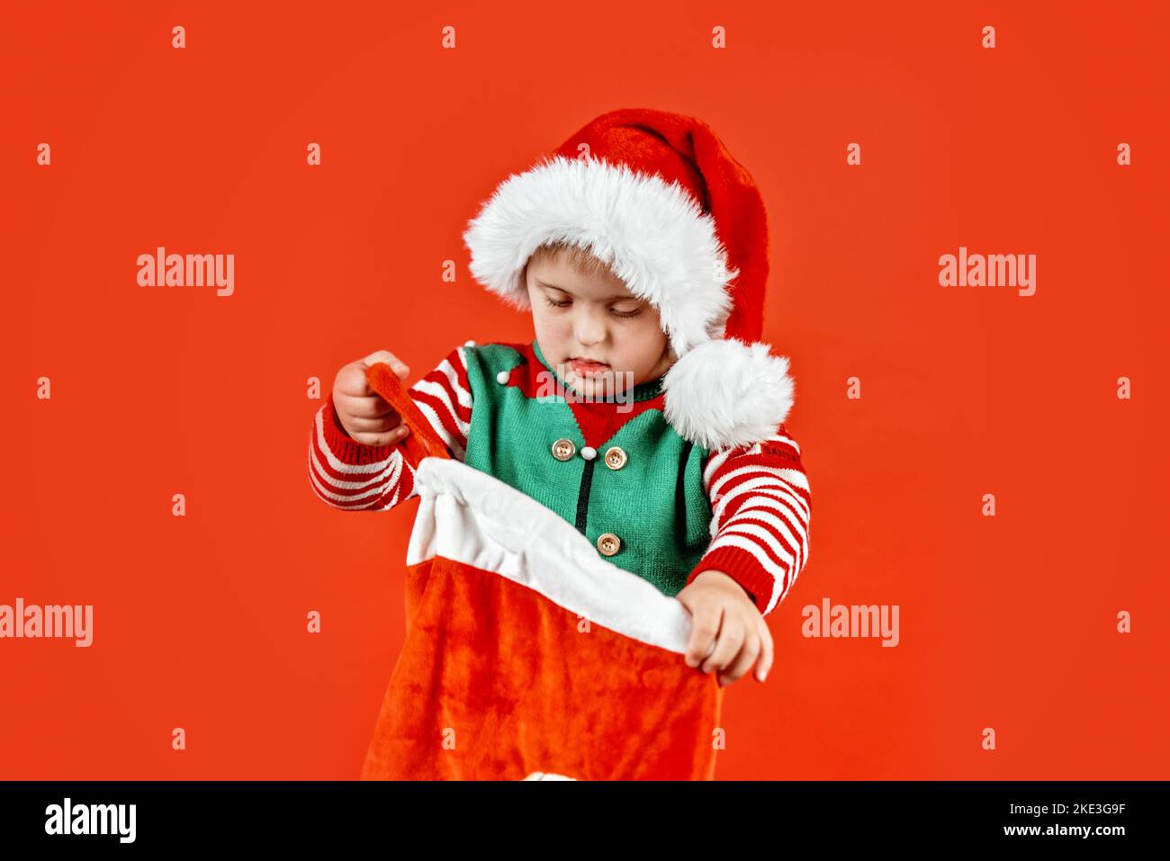 Happy child with Down syndrome in Christmas scarf having fun and laughing in studio. Christmas mood. happy new year. Portrait on red background Stock Photo