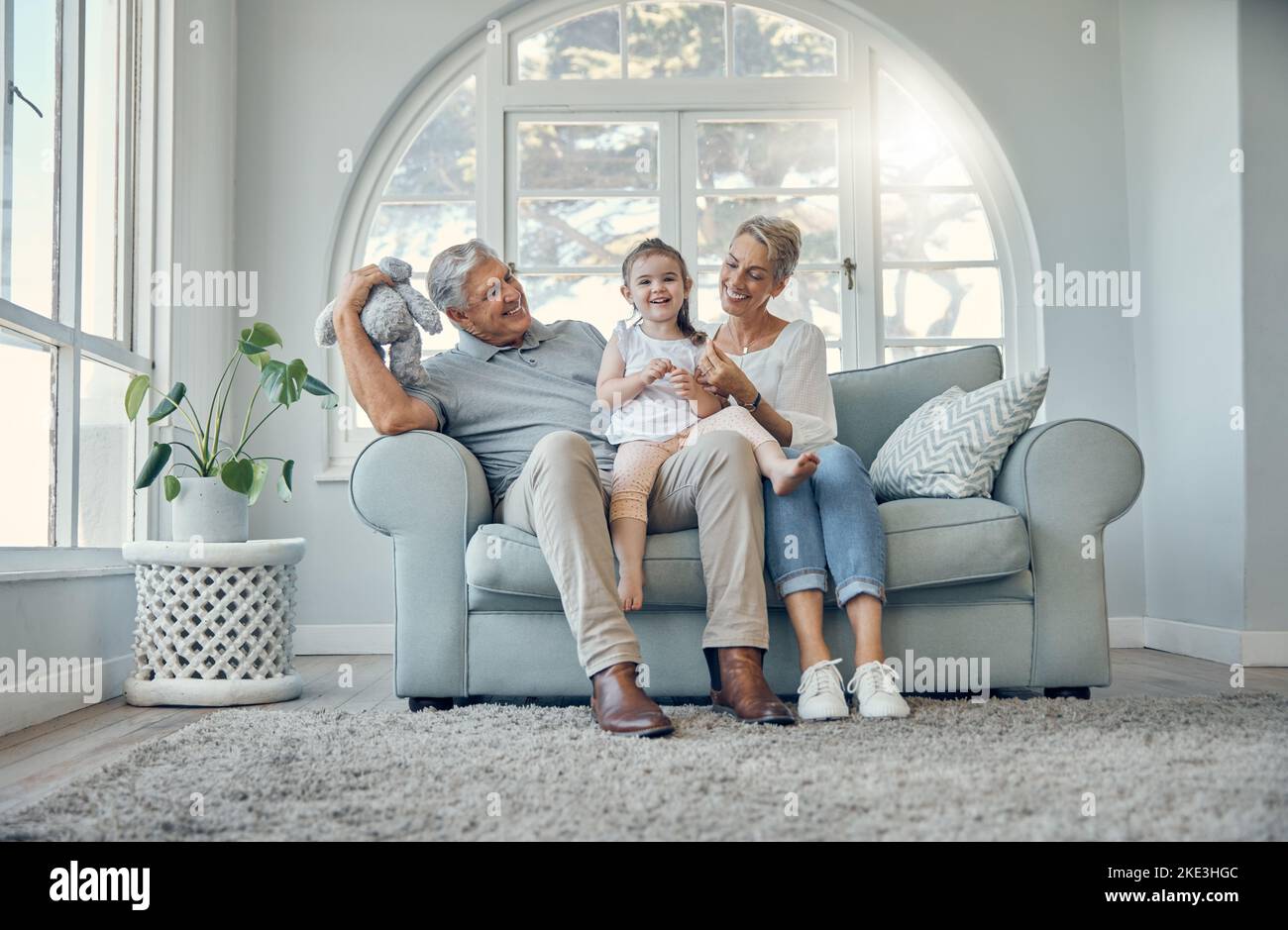 Happy, relax and grandparents with a child on sofa in the living room at family home. Happiness, grandmother, grandfather and girl kid sitting on Stock Photo