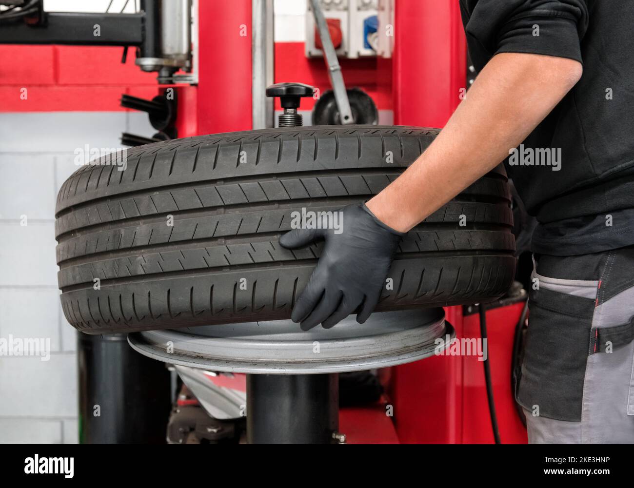 Crop male operator in latex gloves removing tire from wheel barrel during work in dealer shop Stock Photo