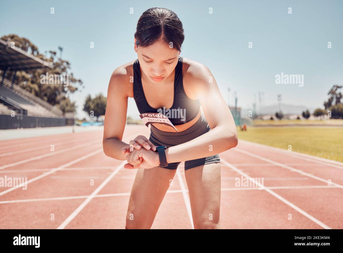 Smartwatch, sports and woman check time, workout goal or progress during training, running or exercise at stadium in summer. Runner, athlete or Stock Photo