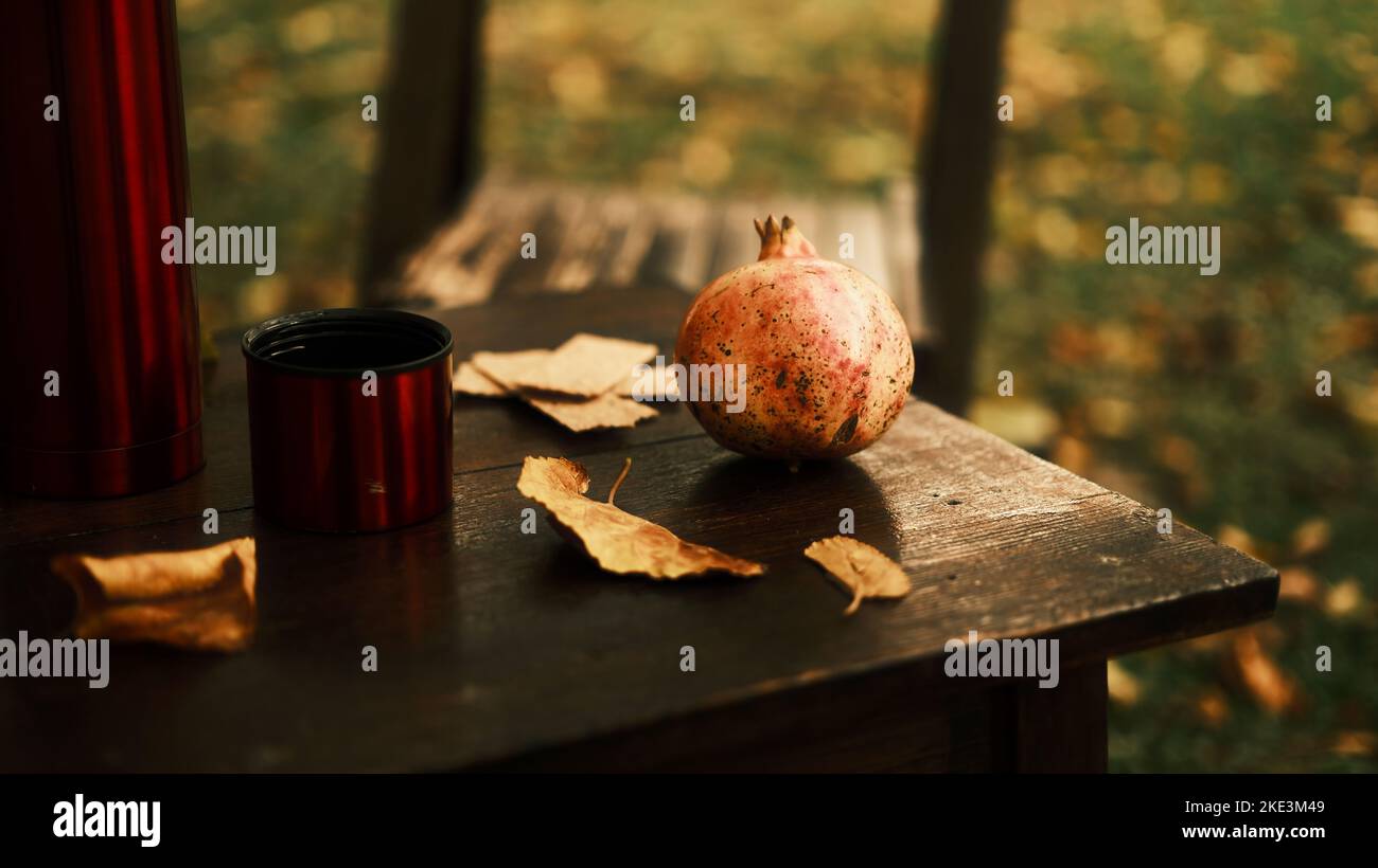 Thermos, mug and pomegranate among autumn leaves on an old, wooden table Stock Photo