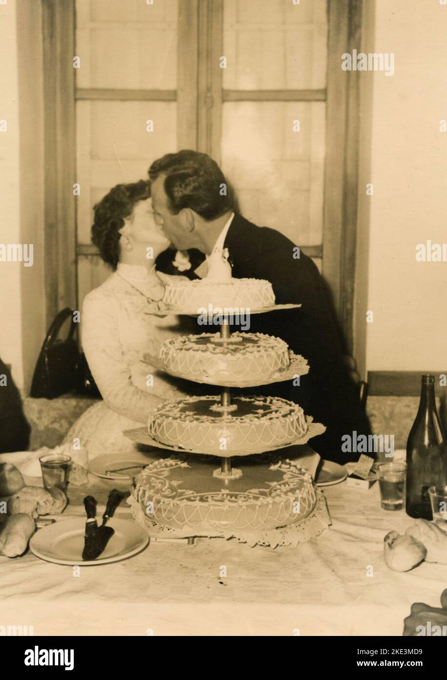 Wedding in a village in central Italy: The Bride and the Groom kissing with the cake, 1950s Stock Photo